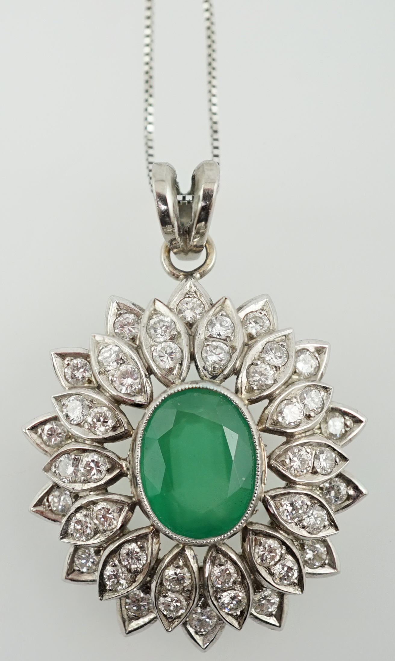 A modern platinum, emerald and diamond cluster set oval pendant